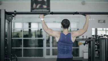 Erkek vücut geliştirmeci yukarı çekerek bir spor salonunda, yakın çekim. Sağa sola ateş dolly (kaymak)