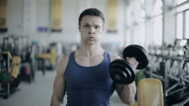 Adam vücut geliştirmeci spor salonunda egzersiz dumbbells ile yürütmek. Tam yüz vurdu