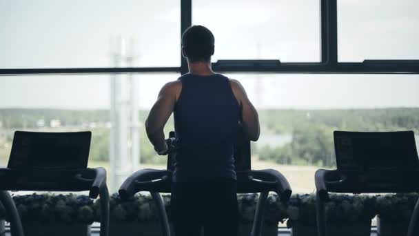 Σιλουέτα του ανθρώπου τρέχοντας treadmill και εξετάζει το μεγάλο παράθυρο. Μέση απόσταση βολής — Αρχείο Βίντεο