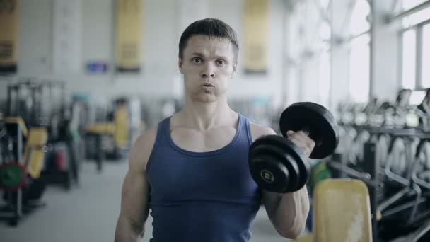 Homme bodybuilder exécuter l'exercice avec haltères dans la salle de gym. Plan complet du visage — Video