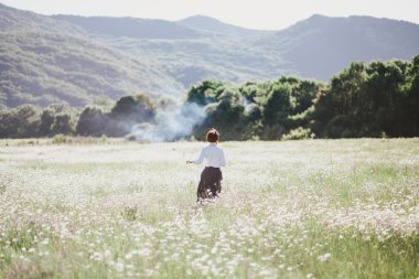 Young beautiful woman enjoying chamomile field among mountains