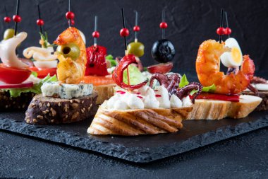 Akdeniz yemeği kavramı - İspanyol tapas - karides, ahtapot, mürekkep balığı, yeşil zeytin, somon, gorgonzola peyniri, üzüm, krem peynir ve kırmızı biberden oluşan sandviçler