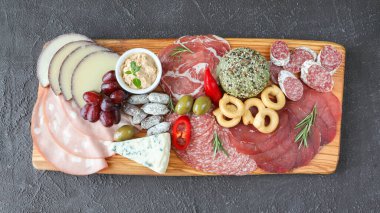 Et tablosu - mortadella, prosciutto, bresaola, gorgonzola, üzümler, taralli, pate, kırmızı biber, yeşil zeytin, biberiye ve fesleğen - siyah zemin üzerinde - fotokopi alanı ve üst görünüm ile yakın plan