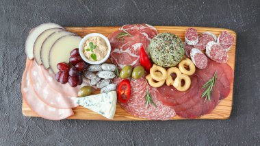 Meat board - mortadella, prosciutto, bresaola, gorgonzola, grapes, taralli, pate, red pepper, green olives, rosemary and basil on a black background - close-up with copy space and top view clipart