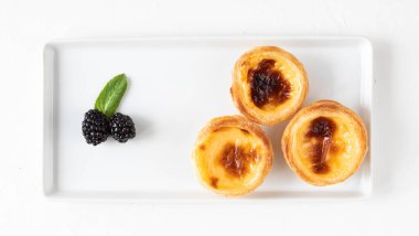 Portekiz ya da Japonya 'nın Pastel de nata pişirmesi - geleneksel kremalı pasta böğürtlenli yumurta sarısı ve beyaz tabakta nane şekeri - üst manzara