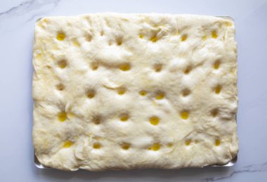 Geleneksel Focaccia hamur un, su, maya, şeker, tuzlu su ve zeytinyağı deliklerinden yapılır - üst görünüm, mermer bir masada pişirme işlemi