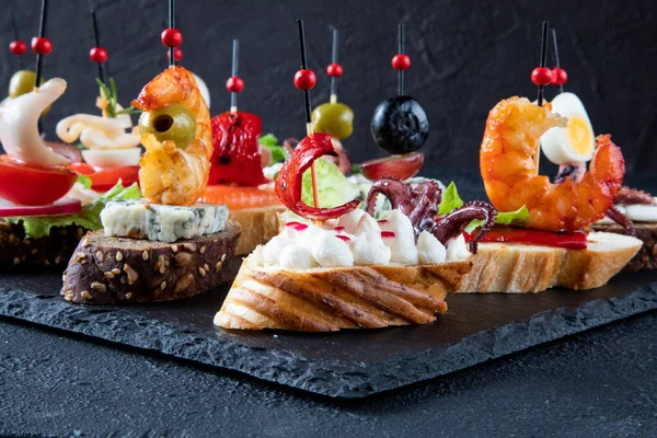 The concept of Mediterranean food - Spanish tapas - sandwiches consisting of shrimp, octopus, squid, green olive, salmon, gorgonzola cheese, grapes, cream cheese, and red pepper