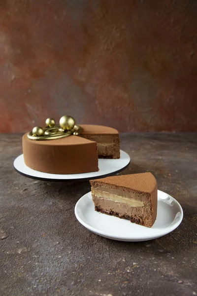 A piece of delicious traditional French mousse cake on a white plate with a large cake in the background, decorated with unusual golden ornaments