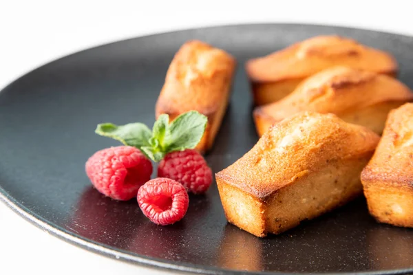 Financier cake - traditional French food on a large, beautiful black plate with raspberries and a mint leaf - a festive concept for Christmas, close-up