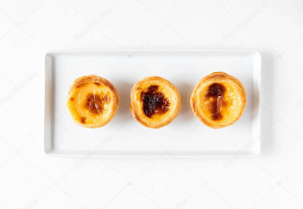 Traditional Portuguese pastry - Pastel de nata on a white rectangular plate on a white table - top view and close-up