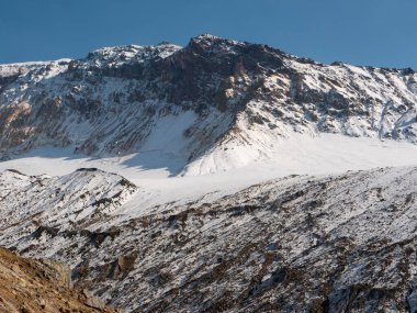 Mutnovsky yanardağına tırmanan turistler. Mutnovsky yanardağının karla kaplı dağlarını mavi gökyüzünün arka planında görüyoruz. Kamçatka Yarımadası, Rusya.