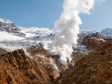 Mutnovsky volkanına tırmanmak. Mutnovsky yanardağının karla kaplı dağlarının manzarası ve fümerollerden mavi gökyüzünün arka planına doğru yayılan buhar. Kamçatka Yarımadası, Rusya.