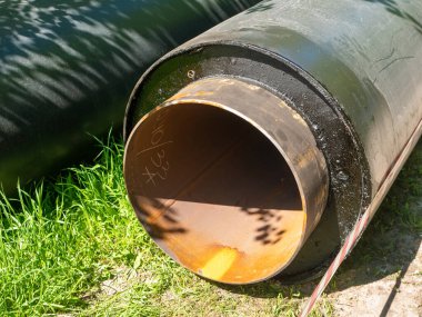 Noyabrsk, Rusya - 5 Haziran 2021: Yeni büyük demir kanalizasyon boruları yerde yatıyor. Siyah borular yeşil çimlerin üzerinde yatıyor ve inşaat bandıyla çevrili..