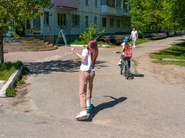 Noyabrsk, Rusya - 5 Haziran 2021: Güneşli bir yaz gününde, insanlar şehir caddesi boyunca yürür. Çocuklar bisiklete ve kaykaya biner, bir adam kaldırım boyunca yürür..