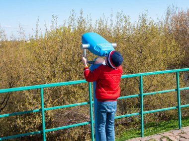 Kolomenskoye Parkı, Moskova 'da güneşli bir bahar günü. Kırmızı ceketli çocuk çitin yakınına monte edilmiş mavi dürbünlerden bakmaya çalışıyor..