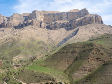Gizhgit Gölü 'nü çevreleyen yüksek kayalık dağları mavi gökyüzü ve yeşil çimlerin arkaplanına bakın. Buraya gelmek için geçilebilir bir araba ve deneyimli bir sürücü gerekir. Elbrus bölgesi, Kafkasya, Rusya.