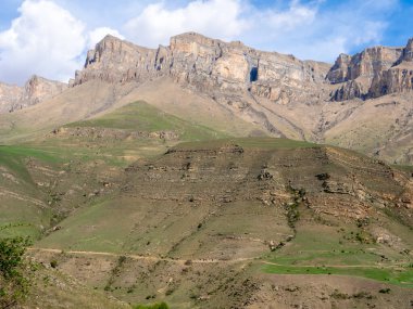 Gizhgit Gölü 'nü çevreleyen yüksek kayalık dağları mavi gökyüzü ve yeşil çimlerin arkaplanına bakın. Buraya gelmek için geçilebilir bir araba ve deneyimli bir sürücü gerekir. Elbrus bölgesi, Kafkasya, Rusya.