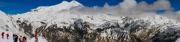 ロシアのエルブラス山 2021年5月10日 青い空に対して雪で覆われたピークを持つエルブラス山のパノラマビュー 人々はチェゴ山を歩き エルブロスの背景を背景に写真を撮る — ストック写真