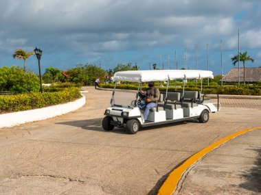 Cayo Coco, Küba, 16 Mayıs 2021: Kübalı bir otelin çalışanı, Club Car 'ı yol boyunca sürüyor. Maskeli adam bir arabanın direksiyonunda oturur ve otelin bahçesindeki başka bir binaya yönelir..