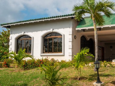 Restoranın İtalyan usulü Tryp Cayo Coco otelinde inşa edilmesi. Tropikal bitkiler yeşil çatılı ve büyük pencereli beyaz bir binanın yanına dikilir. Cayo Adası Coco, Küba.