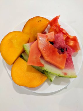 Beyaz bir tabakta dilimlenmiş meyveler. Mango, papaya ve karpuz. Yakın çekim, dikey.