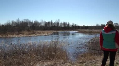 Fotoğraf çeken bir kadın. Sazlıklarla dolu nehir kıyısı. Sakin suyla yavaş akış. 