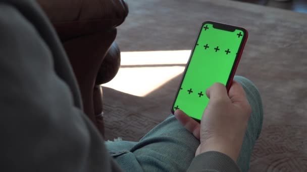 Ruční přejeďte horizontálně displej telefon zelený chromakey. muž sedí na gauči — Stock video
