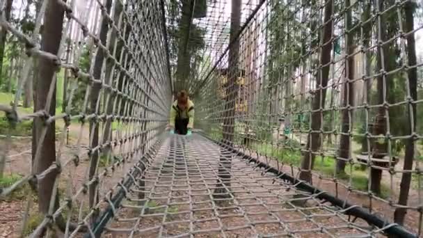Femme grimpant dans un parc à cordes rampant à travers un tunnel à cordes dans la forêt sur les arbres — Video