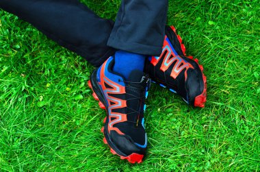 Erkek bacakları kırmızı ve mavi bir çift ayakkabıyla çaprazlanır ve yeşil çimlerin üzerinde uzanır..