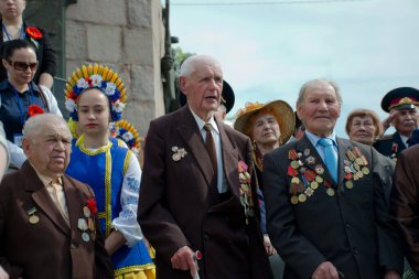 Kherson, Ukrayna - 9 Mayıs 2016: İkinci Dünya Savaşı gazileri, geleneksel Ukrayna kostümü giyen genç bir kızla birlikte bir Zafer Günü töreninde ayakta duruyor.