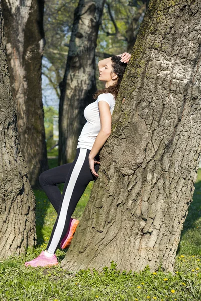 Fitness meisje rusten tegen een boom tussen workouts — Stockfoto