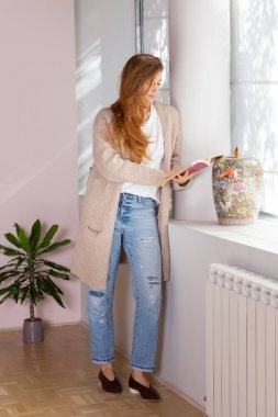 Pencerenin önünde kitap okuyan muhteşem bir kadın.