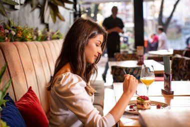 Güzel genç bayan restoranda tek başına meyveli pasta yiyor.