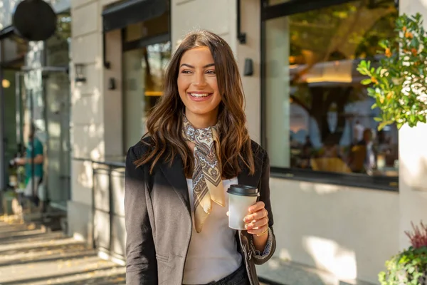 Beautiful woman with cup of coffee walking on street