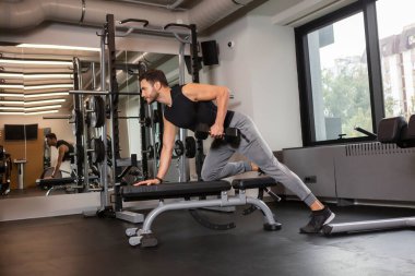 Spor salonunda ağırlık kaldıran kaslı vücut geliştirici adam egzersiz yapıyor.