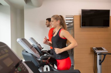 Spor salonunda çalışan, koşu bandında koşan bir çift.