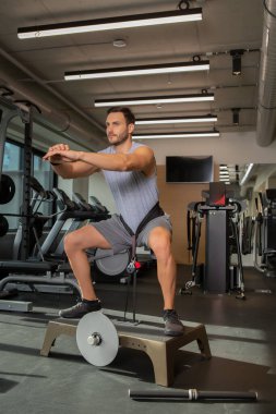 Yakışıklı adam spor salonunda kemerli çömelme yapıyor.