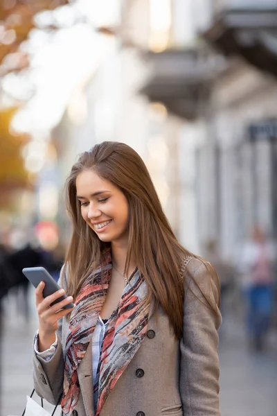 Güzel genç bir kadın sokakta akıllı telefon kullanıyor, gülümsüyor.