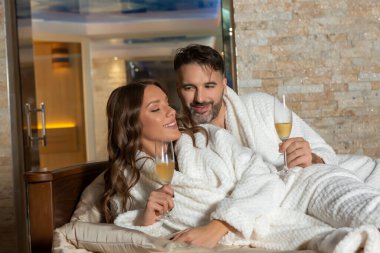Genç ve güzel bir çift, yatakta şarap içiyorlar.