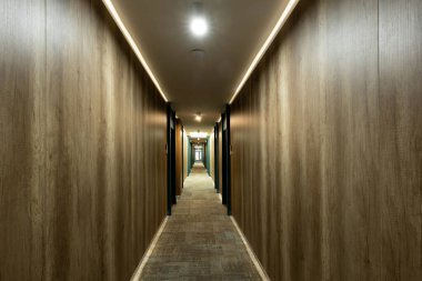 Otel içi, ahşap duvarlı halılı koridor.