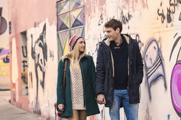 Pareja feliz caminando por la pared de grafitti tomados de la mano — Foto de Stock