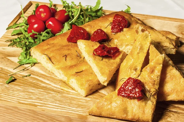 Maïsbrood op een houten bord met gedroogde tomaten en kersen tomatoe — Stockfoto