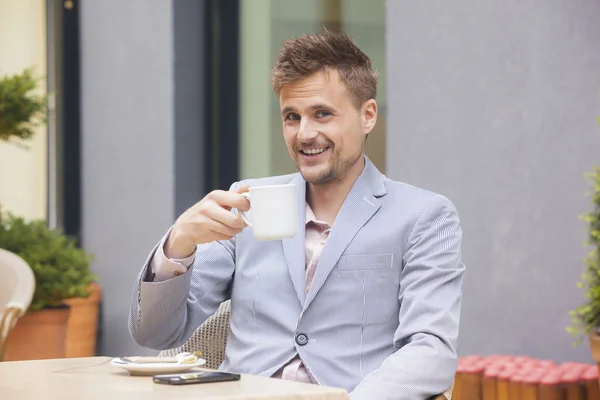 Bonito homem tomando uma xícara de café em um café ao ar livre — Fotografia de Stock