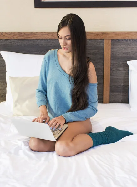 Young woman sitting on bed with laptop — Stock Photo, Image