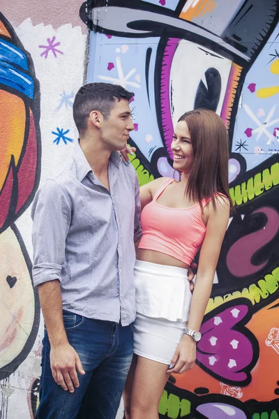 Joven pareja alegre frente a la pared del grafitti —  Fotos de Stock