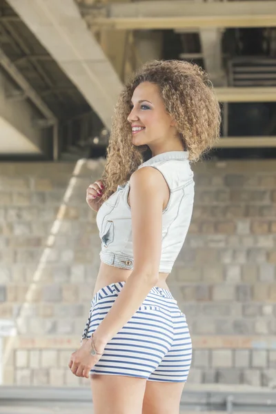 Woman with big curly hair in denim vest and short shorts — Stock Photo, Image