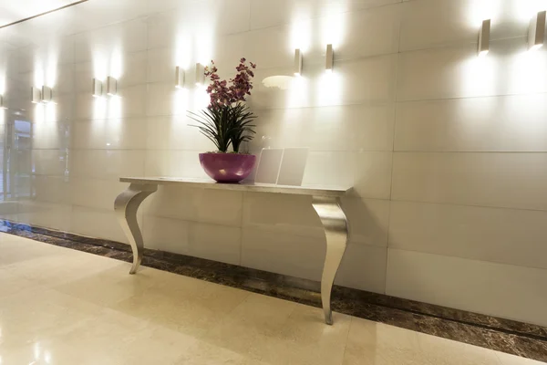 Table and flowers in modern building corridor — Stock Photo, Image