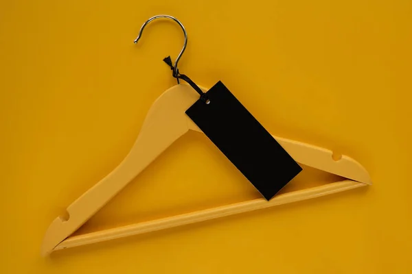 Wooden Coat hanger with black paper label isolated on yellow paper background. Clothing tag, label blank mockup template, to place your design. Black friday final sale banner.