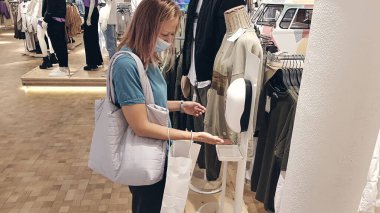 Koruyucu yüz maskesi takan güzel bir kadının portresi, covid-19 salgını sırasında alışveriş merkezinin girişinde dezenfeksiyon için otomatik el dezenfektanı kullanıyor. Yeni normal kasa alışverişi