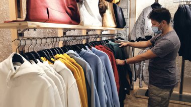 Koruyucu yüz maskesi takan adam, covid-19 salgını sırasında alışveriş merkezinin girişinde otomatik el dezenfektanı kullanıyor. Alışveriş merkezinde yeni normal kasa alışverişi ya da